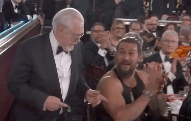 jason momoa in canottiera ai globes con dietro tim cook