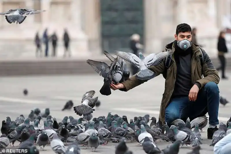 un uomo con la mascherina in mezzo ai piccioni a milano