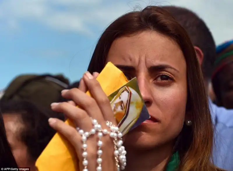 UNA DONNA PREGA SULLA SPIAGGIA DI COPACABANA STRINGENDO UN ROSARIO E DEI SANTINI 