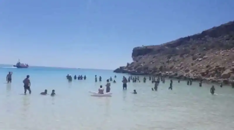 migranti sbarcano sull'isola dei conigli a lampedusa in mezzo ai turisti