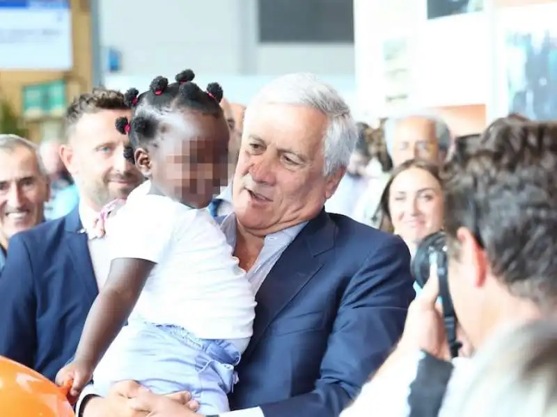 ANTONIO TAJANI AL MEETING DI RIMINI PRENDE IN BRACCIO UNA BAMBINA AFRICANA