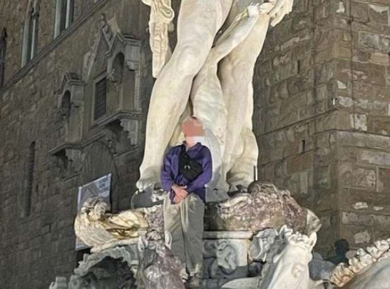 turista tedesco sulla statua del nettuno in piazza della signoria a firenze