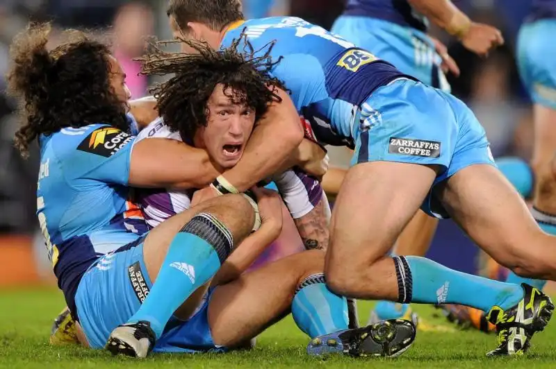 a melbourne storm player screams while getting tackled by gold coast titans players in australia 