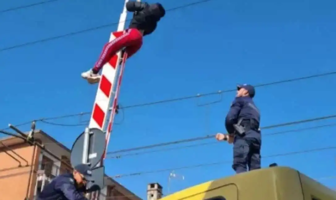 ragazzo aggrappato alla sbarra del passaggio a livello